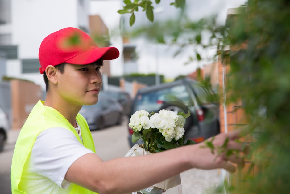 A professional florist wearing a red cap and a neon yellow vest holds a fresh bouquet of white hydrangeas wrapped in white paper. The arrangement features lush, rounded flower heads with vibrant green